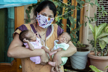 Young indian mother wearing mask holding her two newborn twin babies, new normal lifestyle, Stay...