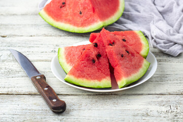 Slices of watermelon on plate with a knife on white wooden background with napkin