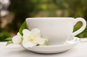 White cup of fragrant tea with a jasmine flower on a white wooden background. Place for text. Side view.