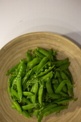 Green peas and an open pea pod in a wooden plate