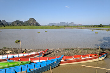 Colorful wooden boats at a lake. Karstic mountains and hills at the background landscape. Mahar Sadan Cave, Myanmar, Burma, South east Asia