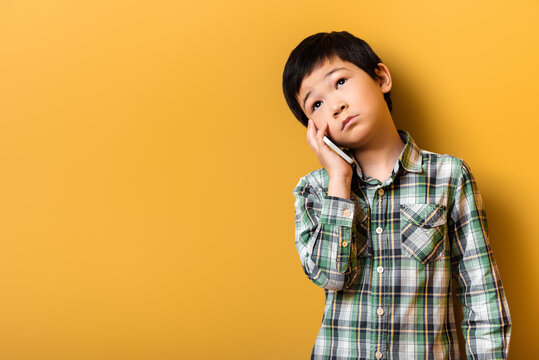 Sad Asian Boy Talking On Smartphone On Yellow