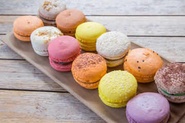 Multi-colored macaroons on a light background. Colorful and tasty macaroons on a plate. Sweet french cookies. Macaroons on wood texture.