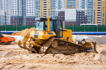 Heavy bulldozer on the construction of sewage and heating communications under the road, amid multi-story residential buildings.