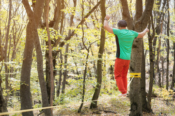 A bearded man aged walks along a slackline in the autumn forest on a sunny afternoon. The concept of Leisure and Recreation of active middle-aged people