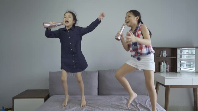 Happy asian sister having fun singing and jumping on bed, pretending and dreaming of become singer in one day, slow motion HD