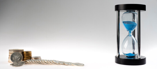 time and money. stacks of coins and an hourglass on a gray background