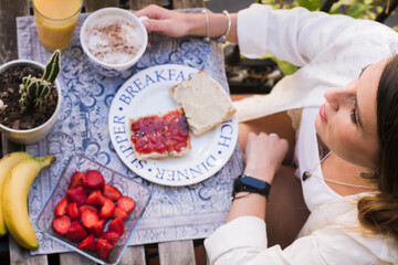 Young girl at breakfast on a balcony. Enjoying the spring time eating healthy fruits and drinking a nice coffee. Sitting, caucasian.