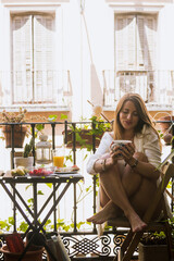 Young girl at breakfast on a balcony. Enjoying the spring time eating healthy fruits and drinking a nice coffee. Sitting, caucasian.