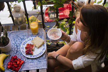Young girl at breakfast on a balcony. Enjoying the spring time eating healthy fruits and drinking a nice coffee. Sitting, caucasian.