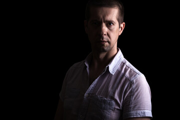 Confident brazen man holds a match in his teeth, in a short-sleeved shirt, looking at the camera, isolated, on black
