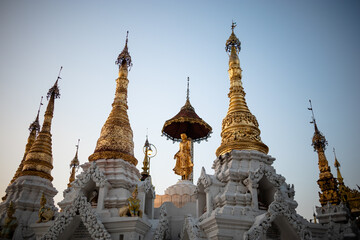 Fototapeta na wymiar White and golden stupas with golden figure at the center. Sunset time. Inside the Shwedagon pagoda. Yangon - Rangoon, Myanmar - Burma, Southeast Asia