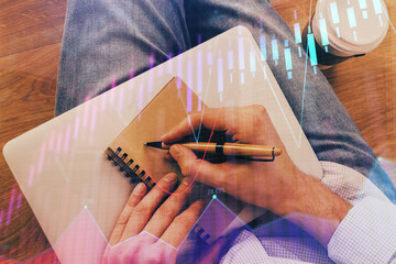 Double exposure of hands writing in notepad with stock market chart.