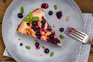 A piece of blackcurrant pie on a grey plate decorated with mint leaves