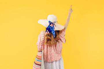 summer young woman in a summer hat, standing with her back to the camera on a yellow background