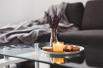 Coffee table design idea: aroma candles and dried lavender bouquet on a metal tray, sofa with grey...