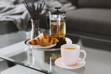 Herbal tea in a pink cup, fresh croissant, french press tea pot and dried lavender bouquet served...