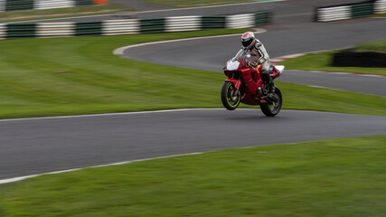 A panning shot of a red racing bike on one wheel as it circuits a track