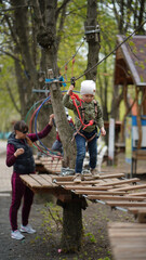 Courageous little boys climbing on a rope bridge with mom's help