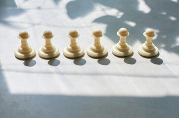 white chess pawns in the sun and their shadow on the table