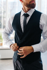 The man dresses by buttoning his vest over his shirt in a close up of his torso arms and chest