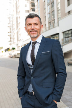 Successful businessman with joyful expression, dressed in formal clothes, stands outdoor near his firm, going to meet with colleagues, looks directly into camera. People, occupation and business