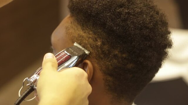 Close up of Young attractive european professional barber making haircut for black man in barbershop. Shaving and cutting hair. modern haircut. Stylish barber shaves an african client