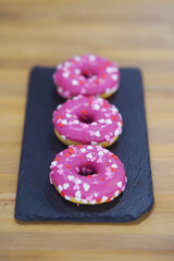 Three Pink donuts on a black tray. Top view