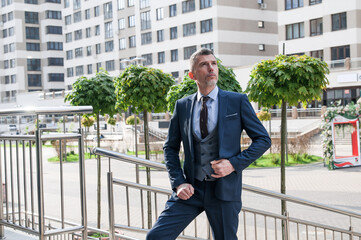 Modern businessman. Confident young man in full suit adjusting his sleeve and looking away while standing outdoors with cityscape in the background