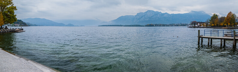 Autumn Alps mountain lake Mondsee misty view, Seepromenade Mondsee, Salzkammergut, Upper Austria. People are unrecognizable.