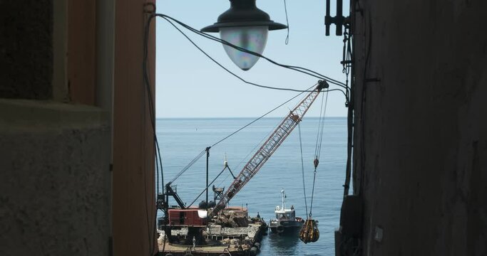 Barge with crane for dredging the seabed at the port of Riomaggiore.Riomaggiore, Cinque Terre, Liguria. Street lamp and barge with crane for dredging the seabed at the port.