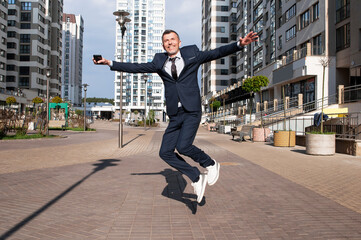 young businessman in a blue suit jumping in the air against blue sky - obrazy, fototapety, plakaty