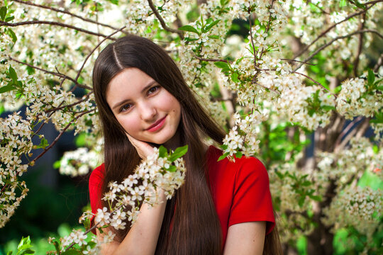 Young teenager girl in red dress against the background of blooming cherry