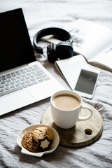 Real home workplace, laptop with cup of coffee with cookies on bed with cozy blanket