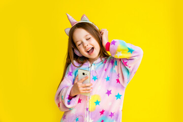 little girl in kigurumi in the form of a unicorn listens to music in headphones and dances on a yellow background. Happy baby in unicorn costume © КРИСТИНА Игумнова