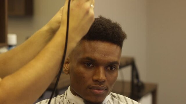 Close up of Young attractive european professional barber making haircut for black man in barbershop. Shaving and cutting hair. modern haircut. Stylish barber shaves an african client