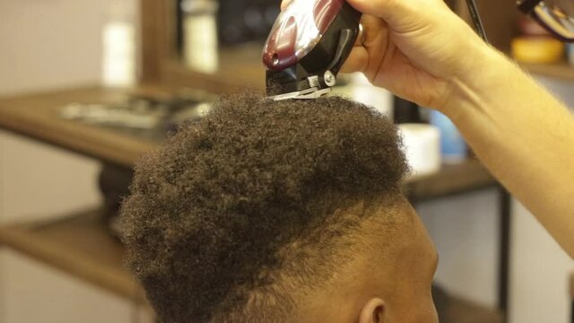 Close up of Young attractive european professional barber making haircut for black man in barbershop. Shaving and cutting hair. modern haircut. Stylish barber shaves an african client