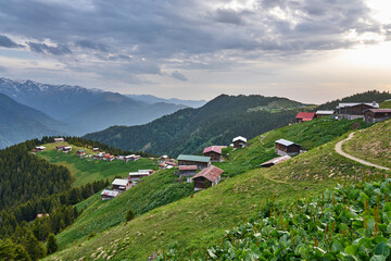 Fototapeta na wymiar Landscape photo of Pokut Plateau with traditional wooden houses, snowy mountains, clouds and forest. Taken in summer at northeastern Black Sea / Karadeniz region of Turkey