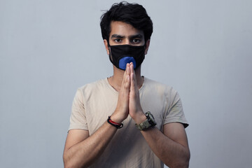 Corona virus concept. Portrait of Indian boy wearing a protective mask against the COVID 19 corona virus, folding his hands requesting to follow the social distancing. 