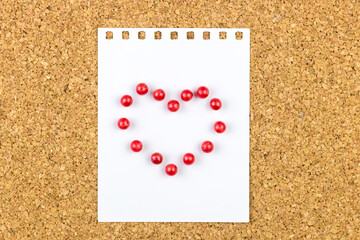 Heart made of red pins attached on a white sheet on a cork board