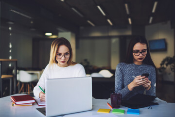 Coworking female colleagues using modern devices while chatting in social network with friends