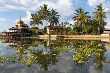 Fototapeta na wymiar Buddhist monastery Nga Phe Kyaung surrounded by vegetation, reflected on the waters of Inle lake, Myanmar, Burma, southeast Asia. Symmetrical picture. Tropical vegetation. Palm trees