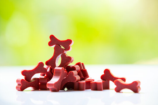 Dog treats are chewy red sticks, bone shaped on white acrylic in bokeh green garden background, Close up shot, Selective focus, Snack for dog, Tooth care