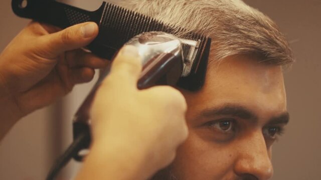 Close up of Hairdresser makes the cut. Fashionable haircut. Barber cuts the beard of a man with razor. Hipster lifestyle. Professional stylist. Portrat view. Man model. Barbershop. Modern Hairstyle