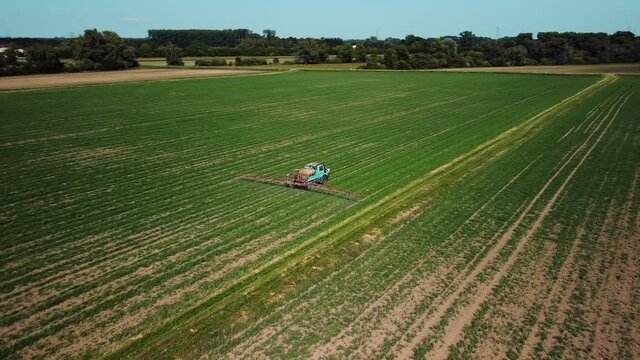 Aerial footage of a tractor watering green fields in western Europe filmed on a sunny day