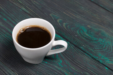 A cup of coffee on brushed pine boards painted in black and green.