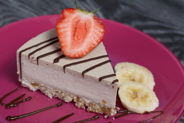 Cheesecake on a plate. Garnished with strawberries, bananas and chocolate. On brushed pine boards painted in black and white.