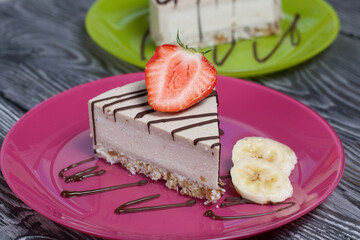 Cheesecake on a plate. Garnished with strawberries, bananas and chocolate. On brushed pine boards painted in black and white.