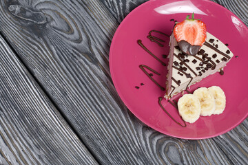 Cheesecake on a plate. Garnished with strawberries, bananas and chocolate. On brushed pine boards painted in black and white.