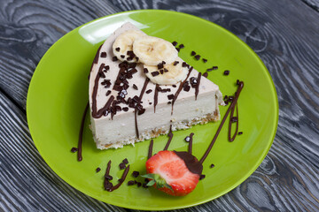 Cheesecake on a plate. Garnished with strawberries, bananas and chocolate. On brushed pine boards painted in black and white.